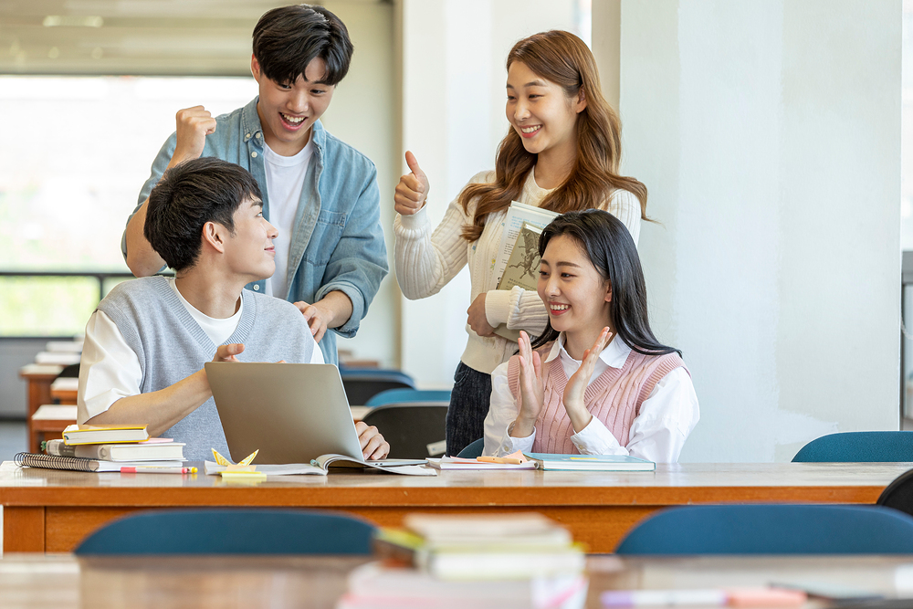 청년일자리도약장려금 신청방법을 논의하는 사람 4명이 있는 이미지. 2명은 책상에 앉아있고, 나머지 2명은 그 뒤에 서 있습니다. 청년일자리도약장려금 신청방법에 대한 내용을 책상위의 노트북에서 확인하고 있습니다.